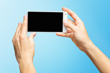 Mockup of female hands holding white frameless cellphone with black screen and making selfie at isolated blue background.