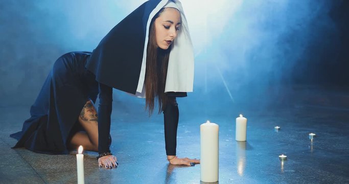 Attractive sexual nun sneaks up to a candle and blows out a candle in a dark smoky studio