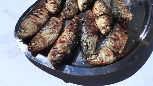 Grilled sardines on a plate with the shadow of some flags moved by the wind