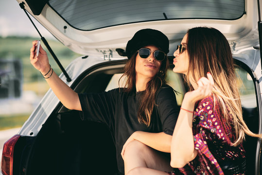 Two women taking selfie while sittink in a trunk. Road rtip concept.