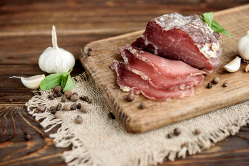 Pork dried meat slices on rustic dark wooden background. Dried pork prosciutto salami ham with herbs.
