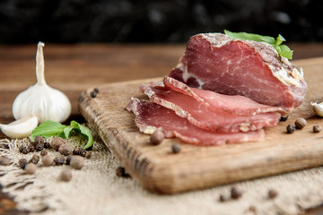 Pork dried meat slices on rustic dark wooden background. Dried pork prosciutto salami ham with herbs.