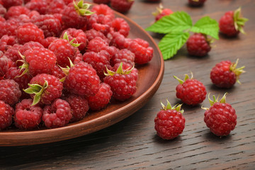 Fruits of red raspberries in a plate and on a table, shot near. Healthy snack