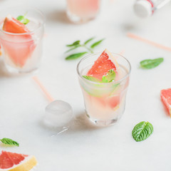 Flat-lay of cold refreshing summer alcohol cocktail with fresh grapefruit, mint leaves and ice over white marble background, selective focus, square crop