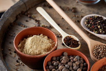 Various spices in wooden spoons and bowls and some salt on an old wooden barrel, top view, close-up, selective focus.
