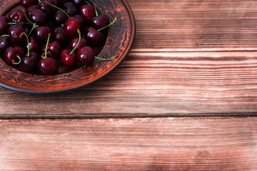 Fresh red cherries fruit on plate on wooden rustic background  with a copy space for text
