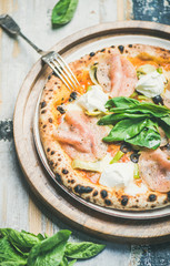Italian lunch or dinner. Freshly baked pizza with artichokes, smoked turkey ham, olives, cream cheese and basil over rustic wooden background, selective focus