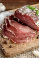 Pork dried meat slices on rustic dark wooden background. Dried pork prosciutto salami ham with herbs.