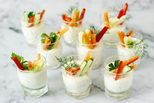 Snack in a glass with fresh cream and various vegetables on a light background.