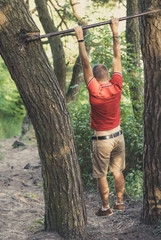 Man hang on the crossbar in the forest 