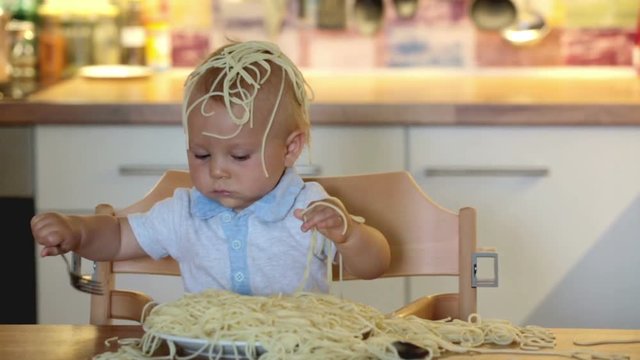 Little baby boy, toddler child, eating spaghetti for lunch and making a mess at home in kitchen