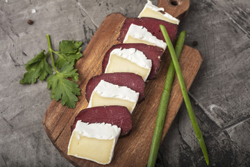 Hardened meat and soft cheese with white mold. Slices of cheese and hardened meat on a wooden board...