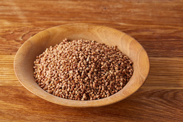 Bowl full of buckwheat grains on rustic wooden table, close-up, selective focus, shallow depth of field.