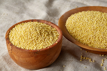 Millet in a wooden bowl on homespun tablecloth, top view, close-up, selective focus.