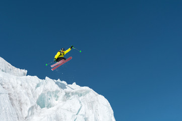 A jumping skier jumping from a glacier against a blue sky high in the mountains. Professional skiing