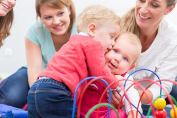 Group of happy young mothers watching their cute and healthy babies while playing with multicolored...
