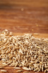 Pile of unpeeled oat grains on wooden background, top view, close-up, macro, selective focus.