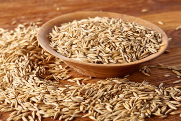 Pile of unpeeled oat grains on wooden background, top view, close-up, macro, selective focus.