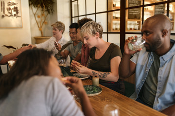 Young friends eating and drinking together at a bistro table