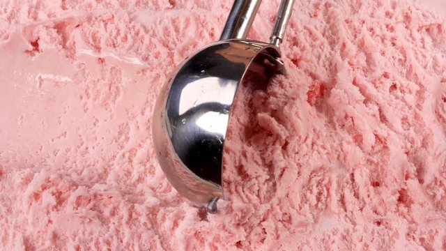 Strawberry ice cream scooped out of container with a utensil. Closeup 4k