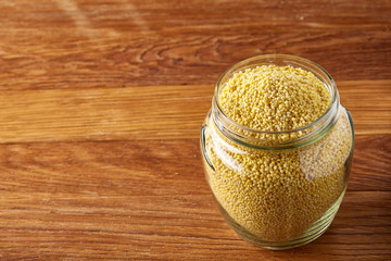 Raw organic natural millet in glass jar on a wooden table, horizontal, copy space, close-up.