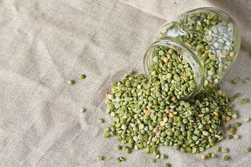 Raw green peas in glass jar on homespun tablecloth, close-up, selective focus.