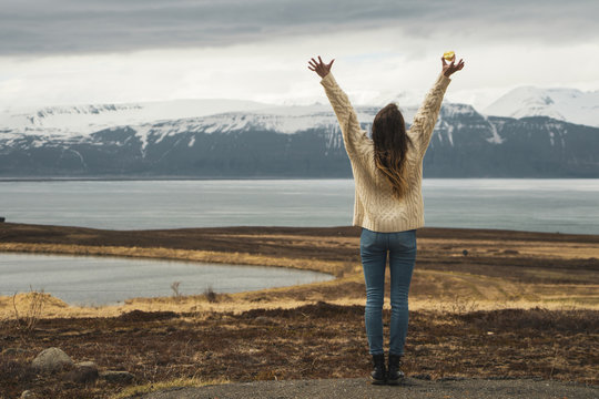 Iceland, woman standing at lakeside with raised arms