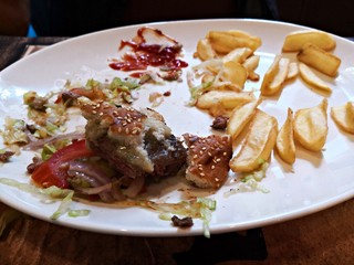 Food scrap on a plate at the restaurant: burger, fries, vegetables and red sauce.