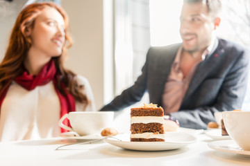 Obraz na płótnie Canvas Delicious layered cake served with coffee on the table of a young couple in love during romantic date in a trendy cafeteria