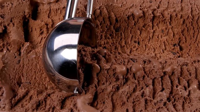 Chocolate ice cream scooped out of container with a spoon. Closeup 4k