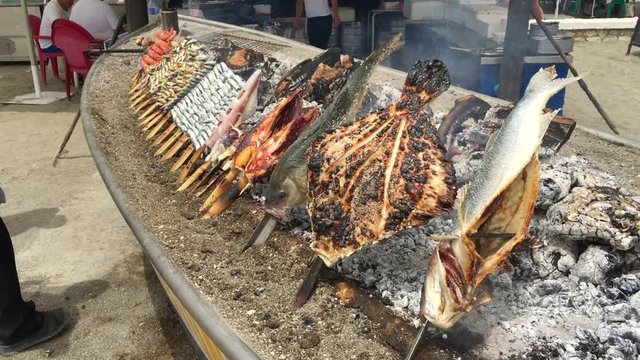 Sardine, shrimp, squid on sticks on fire are fried in a boat. Typical "espetos" food of Spain, Costa del Sol, Malaga. Traditional food.