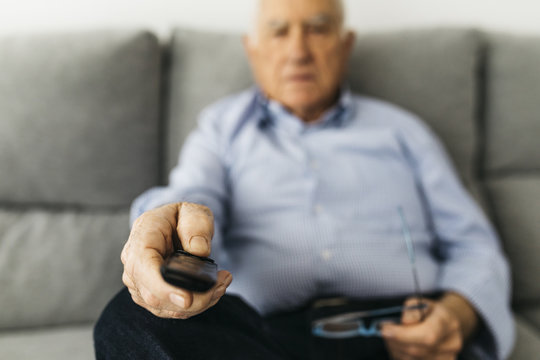 Senior man watching TV from the couch at home, focused on hand