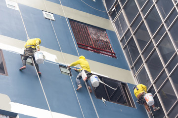 painters hanging on roll, painting color on building wall.