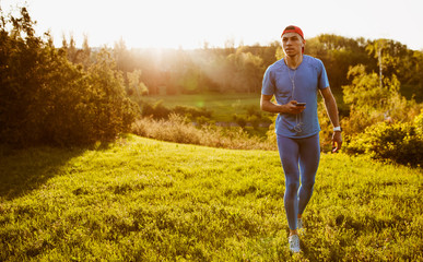 Young fit male runner exercising on green grass in the park. Horizontal shot of handosme athlete running and sprinting outdoor preparing for marathon. Sport and people concept.