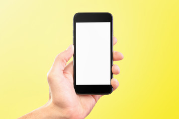 Male hand holding black cellphone isolated at yellow background.
