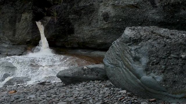 The waterfall flows from the rock to the stone beach. Shevelev.