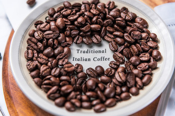 Traditional Italian Coffee beans are scattered around a white saucer and wooden chopping board.