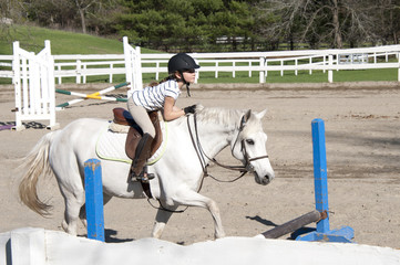 Young girl on white horse at horseback riding lesson. 