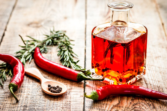 Bottle with chili oil and herbs on wooden background