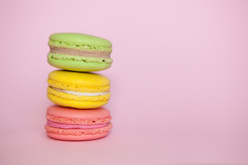 Green, yellow and pink Macaroon biscuits on pastel pink background with copy space