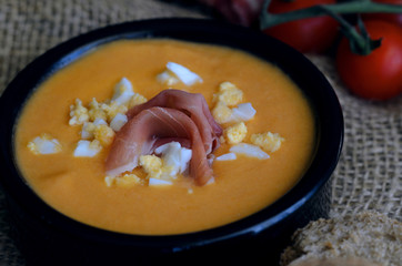 Close up of Salmorejo, creamy cold tomato soup, served with serrano ham and hard-boiled eggs.