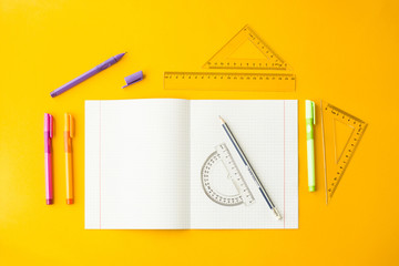 Notebook in a cell among pens, pencils and rulers on a yellow background. Accessories for study....