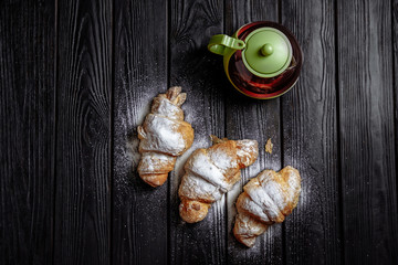 three croissants with tea on dark wooden background close-up top view