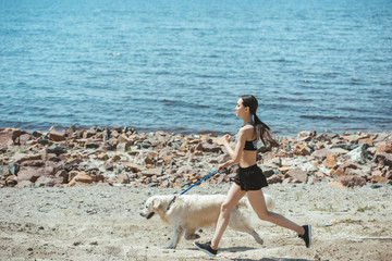 side view of asian sportswoman jogging with dog on beach