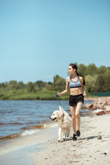 attractive young asian sportswoman running with golden retriever near sea