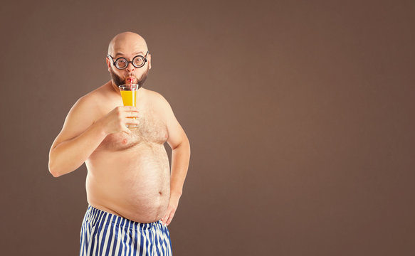 A funny fat man with a naked stomach drinks juice on a summer vacation.
