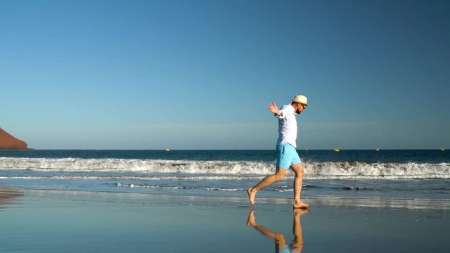 Happy man runs along the ocean beach at sunset. Concept of carefree modern life. Tenerife, Canarian Islands. Slow motion
