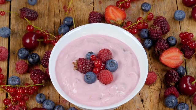 Forest fruits yogurt in bowl rotating on table full of fresh fruits. Healthy breakfast eating concept. 4k