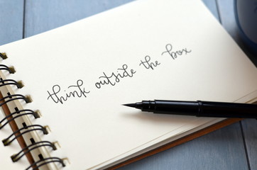 THINK OUTSIDE THE BOX hand-lettered in notebook with cup of coffee on desk