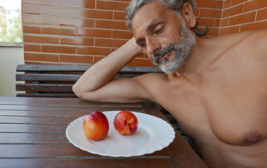 healty mature man sitting at kitchen table  with peach fruits